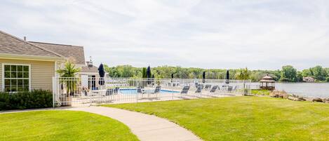 A pool area with lounge chairs and a gazebo, surrounded by a white fence and a pathway.