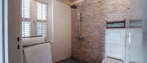 A bathroom with a shower, toilet, and a window with blinds.
