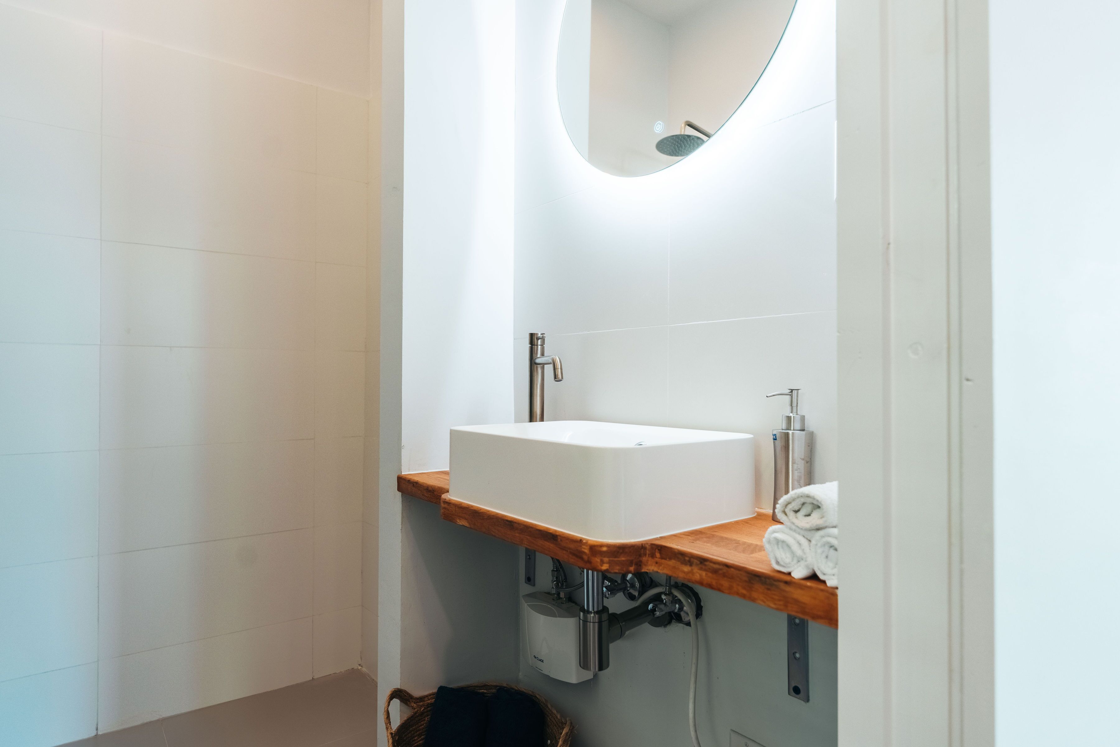 A modern bathroom with a white sink, wooden countertop, and a round mirror.