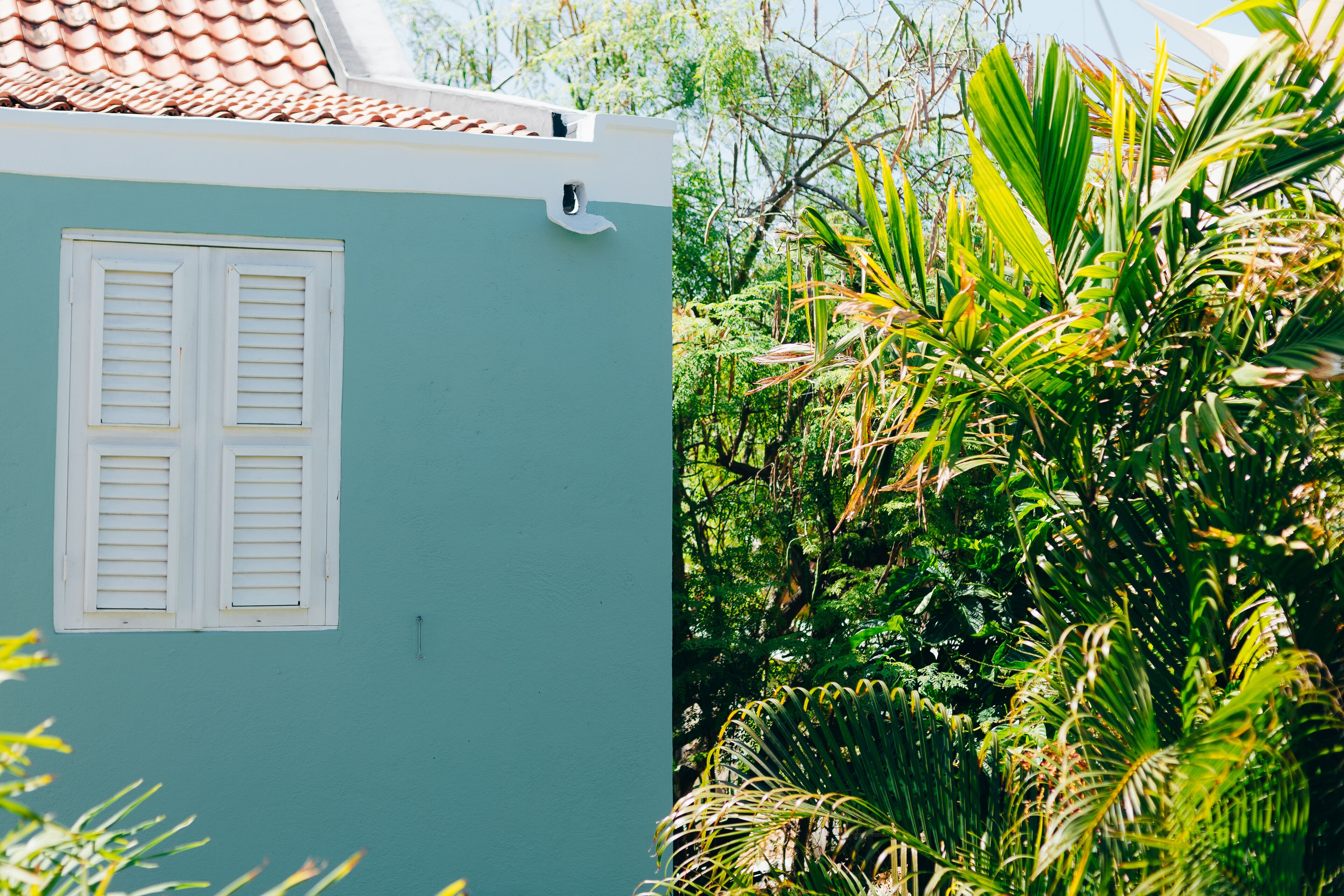 Un bâtiment à la façade de couleur turquoise, avec des volets blancs et un toit recouvert de tuiles.
