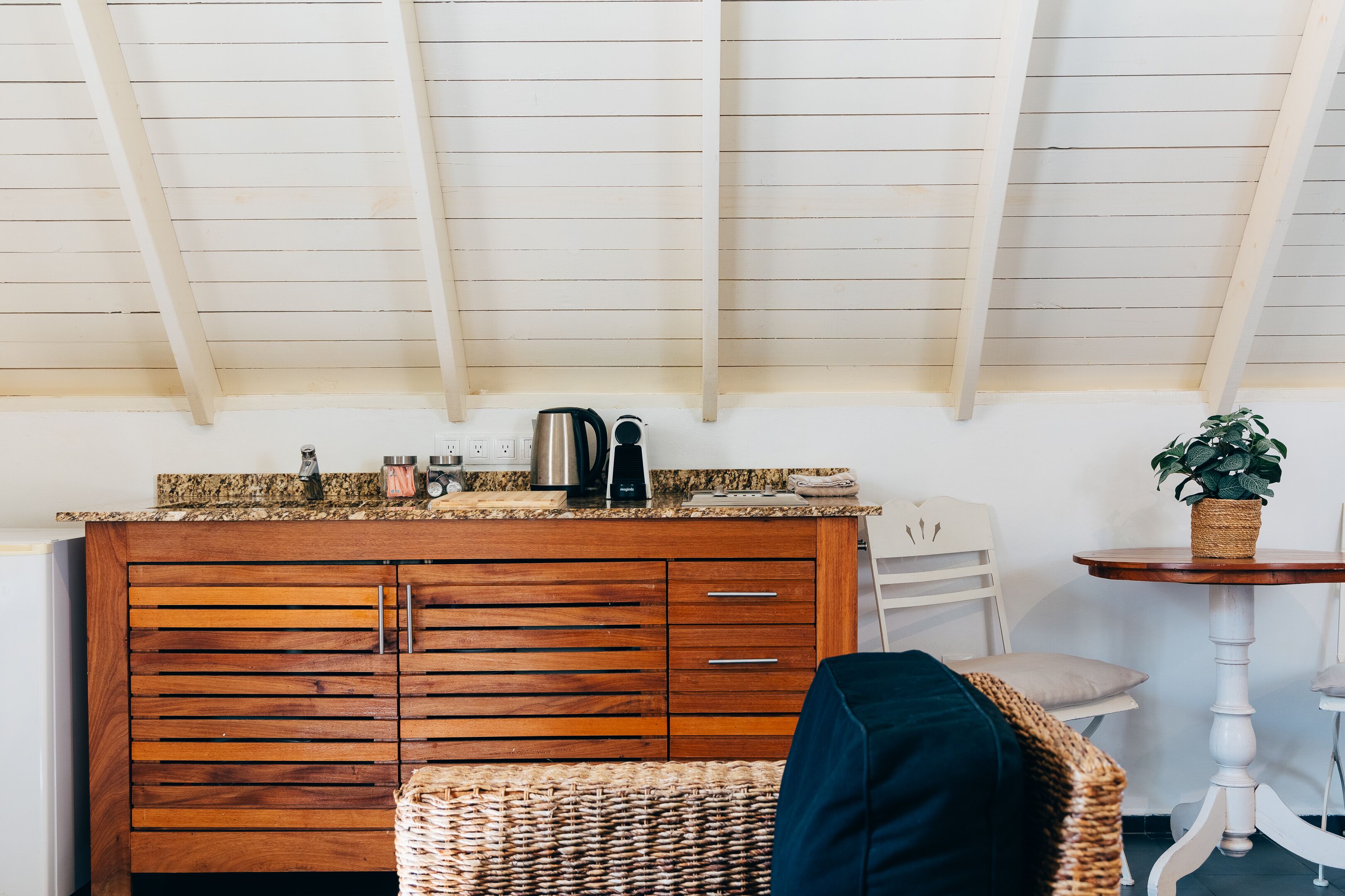 A kitchen with wooden cabinets, a coffee maker, and a plant on a small table.