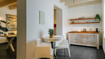 A modern kitchen with white cabinetry, a round dining table, and chairs. There are shelves with dishes and a potted plant.