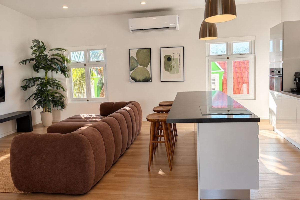 Una cocina moderna con una isla central, un área de comedor con un sofá marrón grande y una planta en maceta.