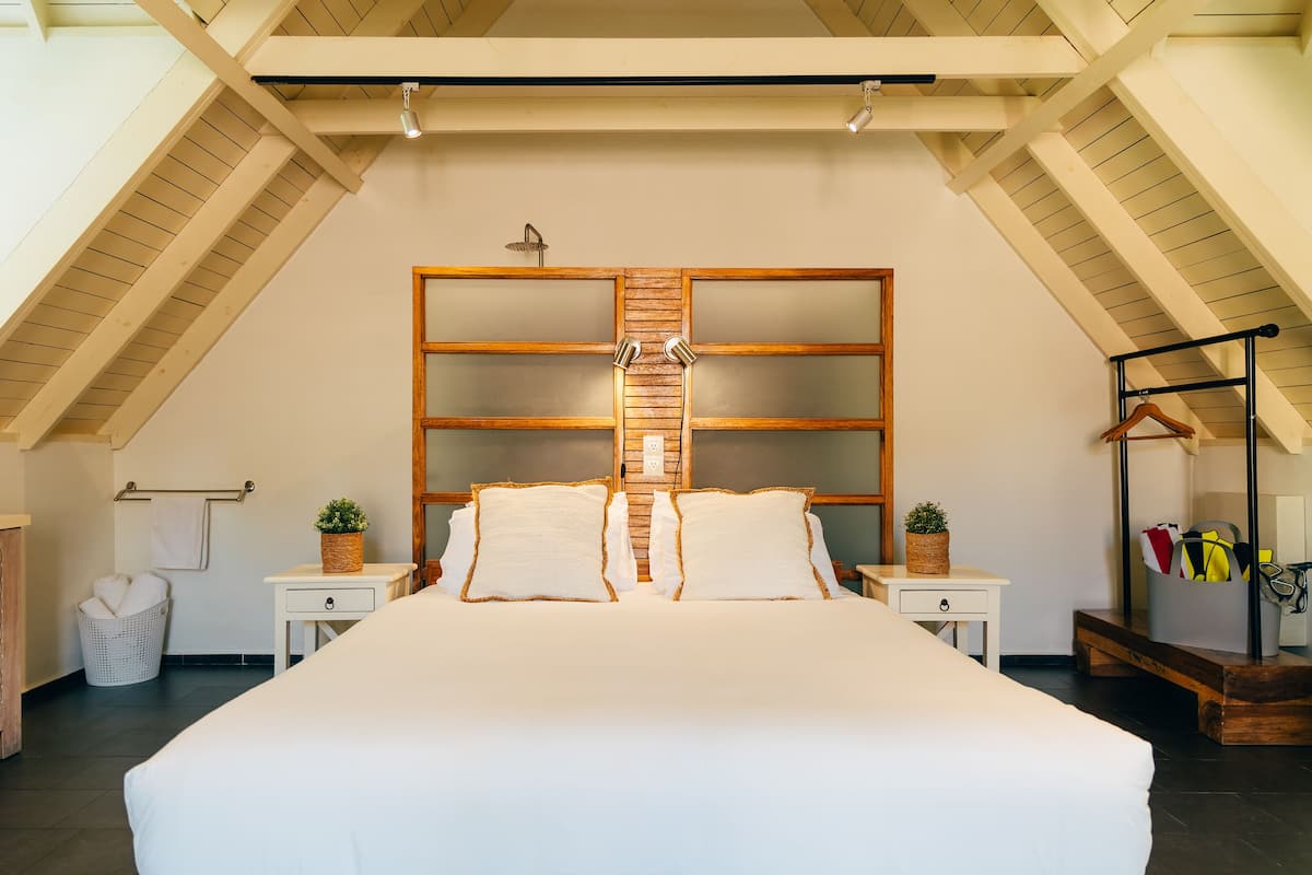 A bedroom with a large bed, wooden headboard, bedside tables, a hanging coat rack, and a small bench.