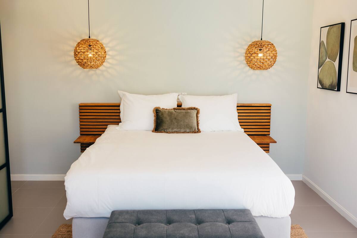 A neatly arranged bedroom with a large bed, two bedside tables, and two hanging spherical lamps.