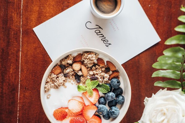 Un tazón de yogur con almendras, granola, fresas y arándanos sobre una mesa de madera.