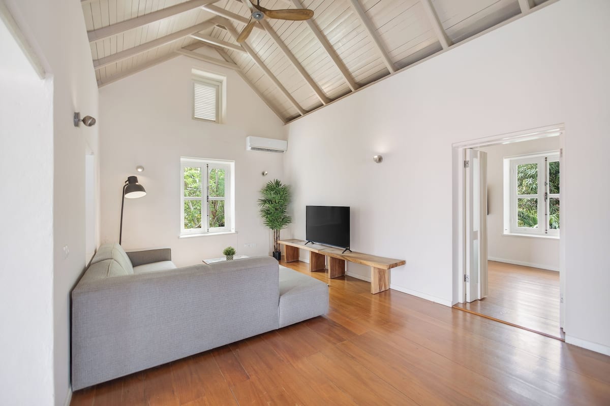 A spacious living area with a sofa, TV, wooden bench, and large windows.