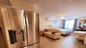 Una cucina moderna con frigorifero in acciaio inossidabile, zona pranzo con tavolo e sedie, divano e un letto sullo sfondo.