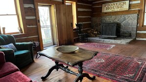 L’intérieur d’un chalet confortable, avec des murs en rondins de bois, une table en bois, des fauteuils rouges moelleux, une cheminée en pierre et une pancarte indiquant : « Pioneer House, Mme L. Griffin ».