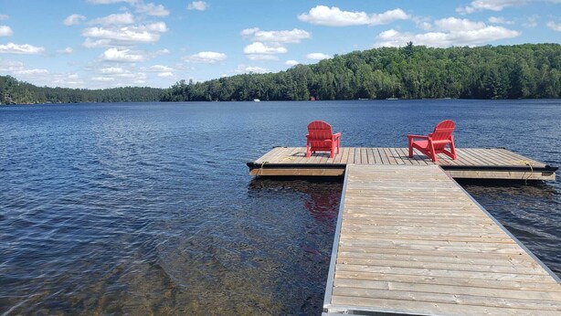 Une jetée en bois s’avance sur un lac paisible, et deux chaises rouges sont placées face à l’eau.
