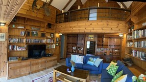 Un salon spacieux avec une grande télévision, des étagères à livres, un canapé bleu et un plafond en bois.