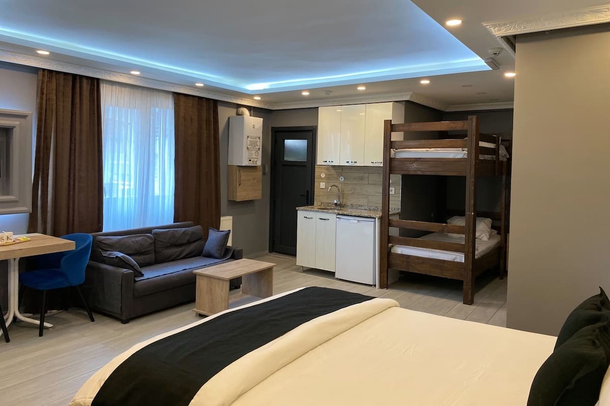 A compact hotel room with a bed, a sofa, a desk, and a kitchenette.