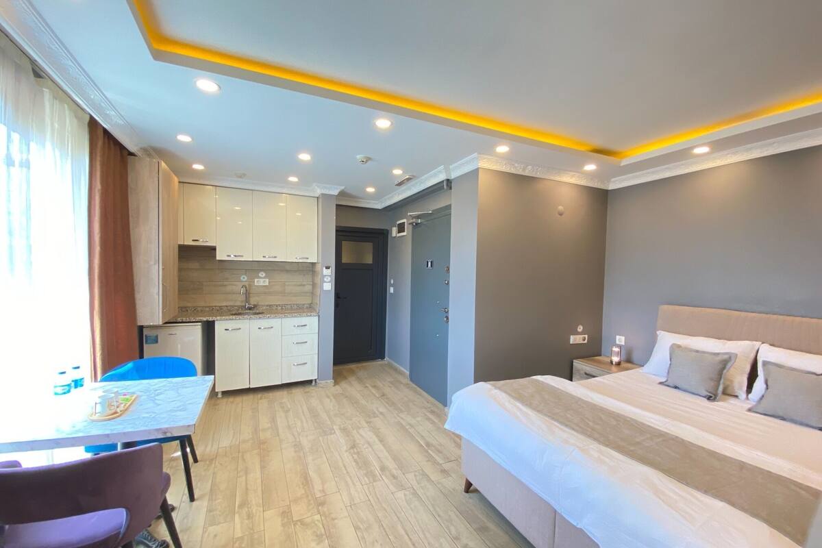A compact hotel room with a bed, a small desk, and a kitchenette.