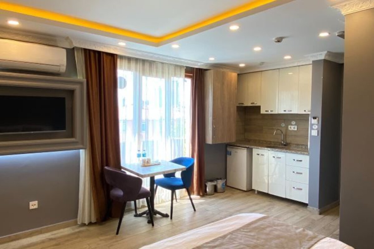Une cuisine compacte dotée d’appareils électroménagers modernes, un coin repas avec deux chaises et une grande fenêtre avec des rideaux.