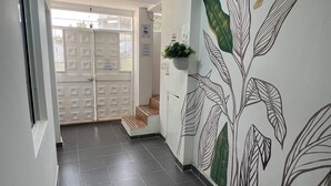 Un pasillo con suelo de baldosas, una puerta con diseño geométrico y una pared con un mural de hojas y pájaros.