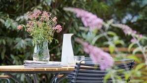 Uma mesa com um vaso de flores cor-de-rosa, um jarro branco e um copo.