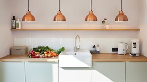 Cozinha moderna com pia branca, luminárias pendentes de cobre, bancada de madeira e cafeteira.