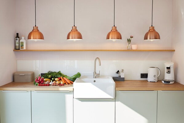Una cocina moderna con un lavamanos blanco, lámparas colgantes de cobre, encimera de madera y una cafetera.