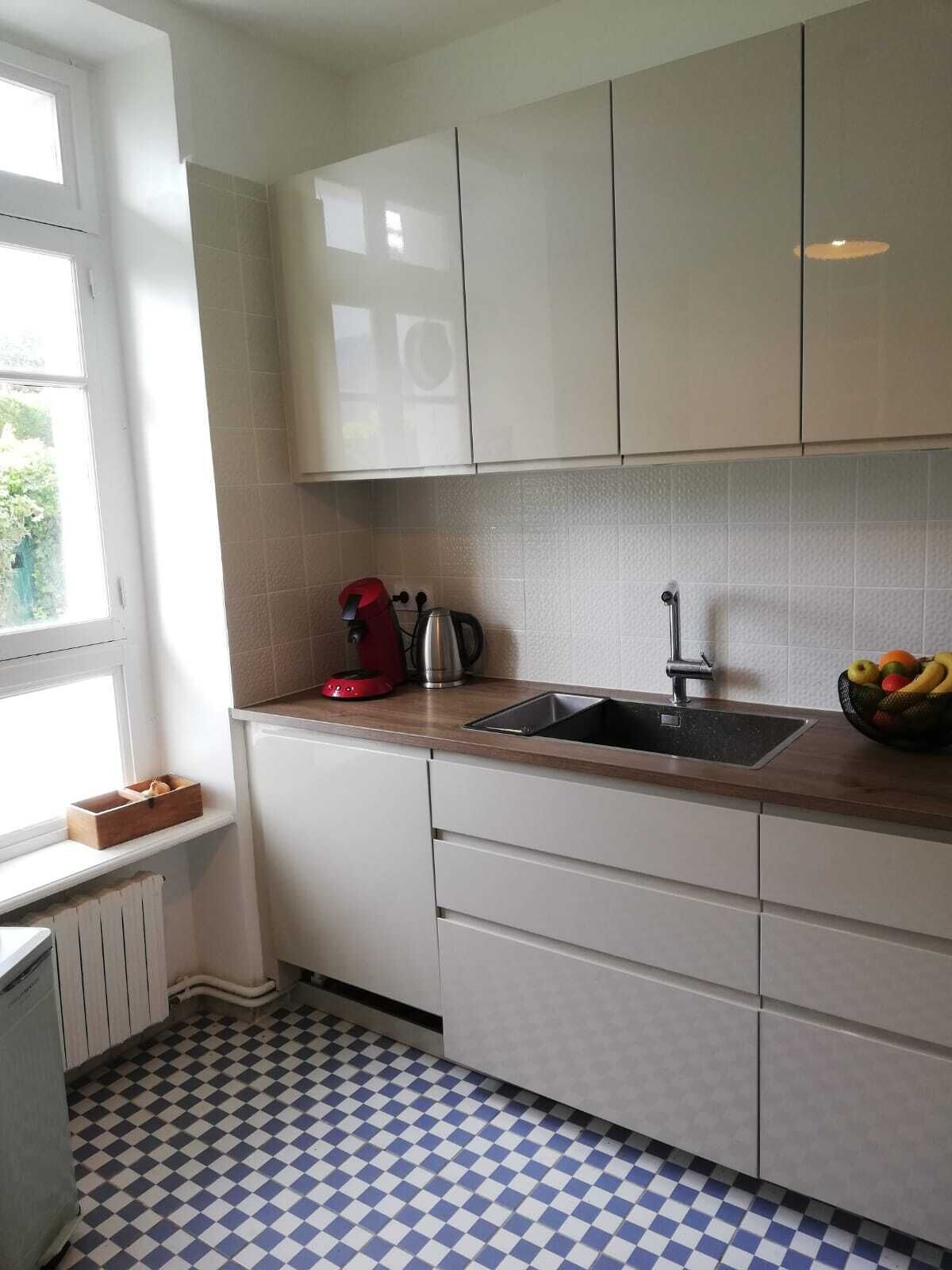 A kitchen with white cabinets, a black sink, a red kettle, and a fruit bowl on the counter.