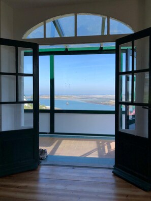 A room with a large bay window, wooden flooring, and a view of the sea.