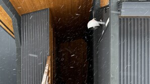 Una escalera de madera que conduce a un interior oscuro, rodeada de paneles metálicos y nieve.