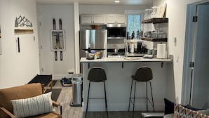 Una cocina moderna con armarios blancos, un refrigerador de acero inoxidable y una barra con taburetes.