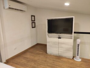 A room with a white cabinet, a flat-screen TV, and a standing fan.
