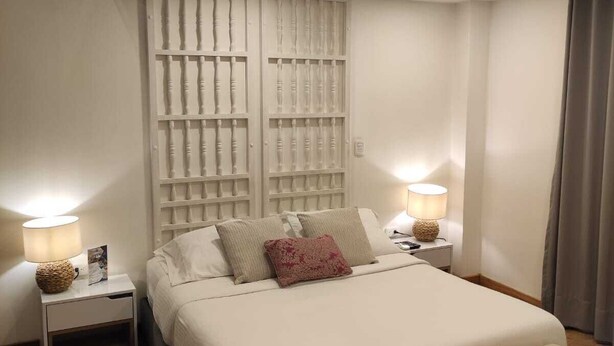 Un dormitorio moderno con una cama grande, mesitas de noche con lámparas, un banco y un panel decorativo en la pared.