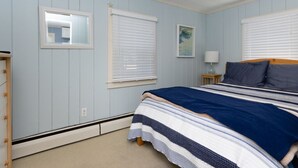 A bedroom with a bed, a nightstand, a lamp, and a window with blinds. - Quintessential Cape Cottage. Block from the beach (Falmouth)
