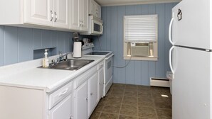 A compact kitchen with white cabinets, a microwave, a sink, and a refrigerator. - Quintessential Cape Cottage. Block from the beach (Falmouth)