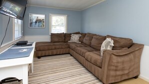 A living room with a brown sectional sofa, a white desk, and a striped rug. - Quintessential Cape Cottage. Block from the beach (Falmouth)