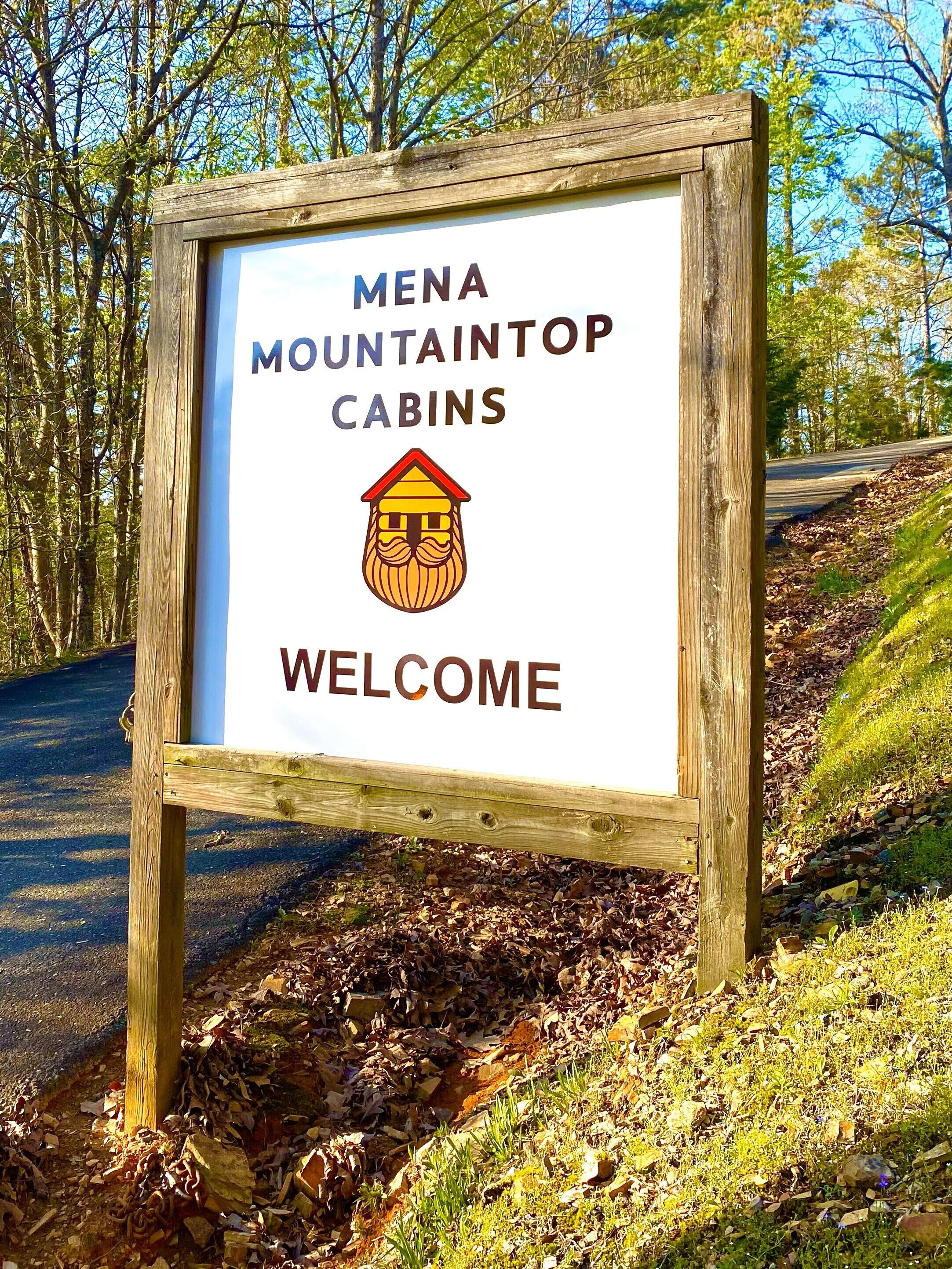 A wooden sign with the text "MENA MOUNTAINTOP CABINS" and a graphic of a cabin, welcoming visitors.