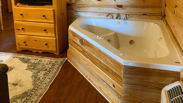 A wooden cabin interior with a wooden dresser, a television, and a large bathtub.