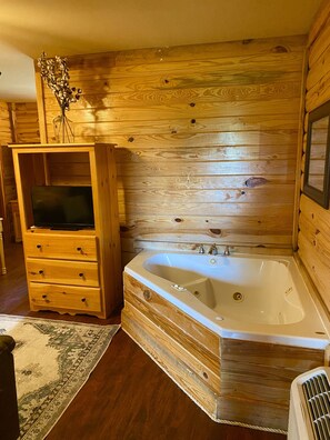 A wooden cabin interior with a wooden dresser, a television, and a large bathtub.
