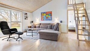 Een ruime woonkamer met een hoge plafond, een bank, een salontafel en een stoel. Er hangt een schilderij aan de muur en er staat een houten ladder in de hoek.