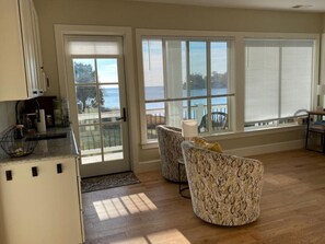 A kitchen with a refrigerator, a dining area with two patterned chairs, and a view through large windows.