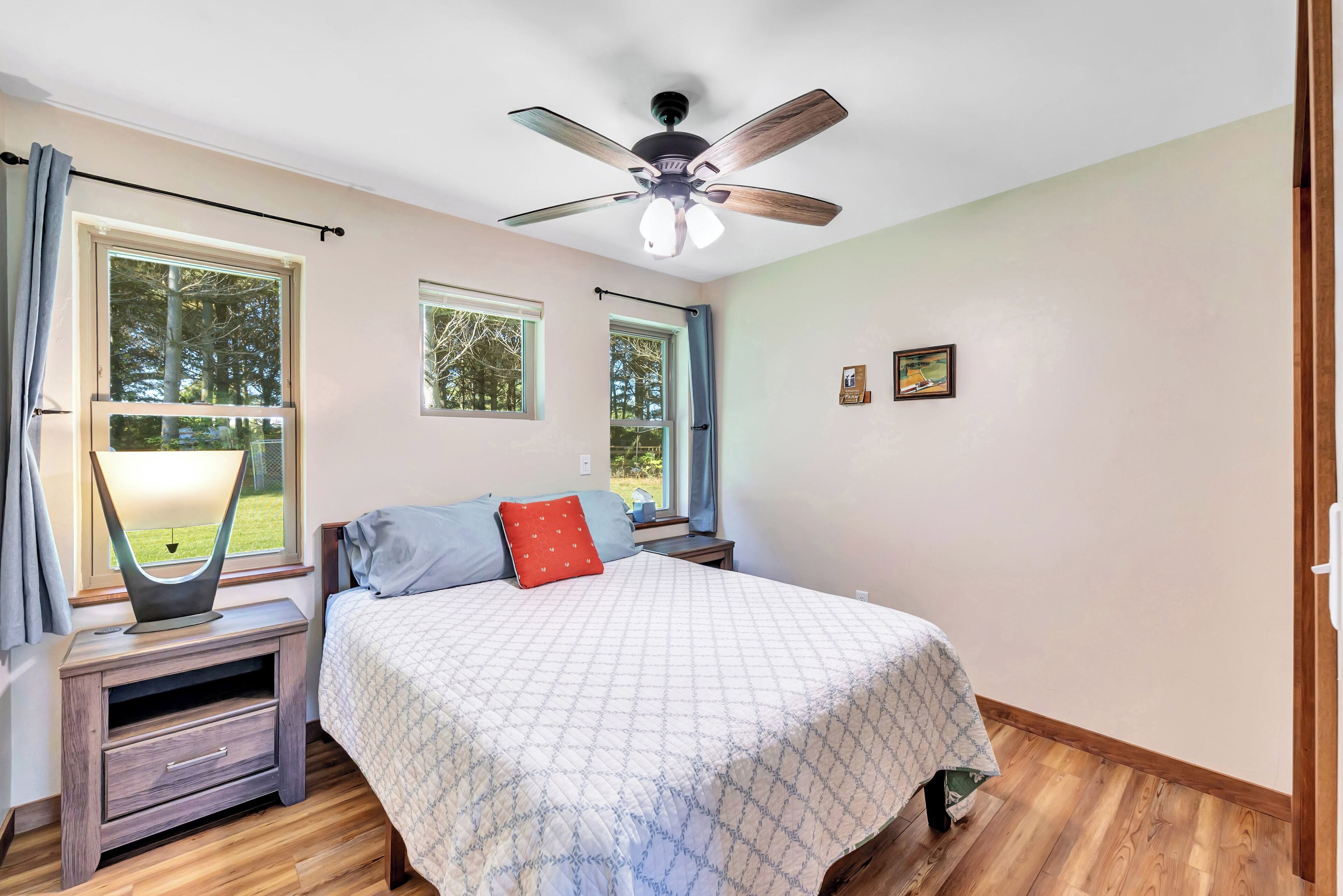 A bedroom with a bed, nightstand, lamp, ceiling fan, and windows.