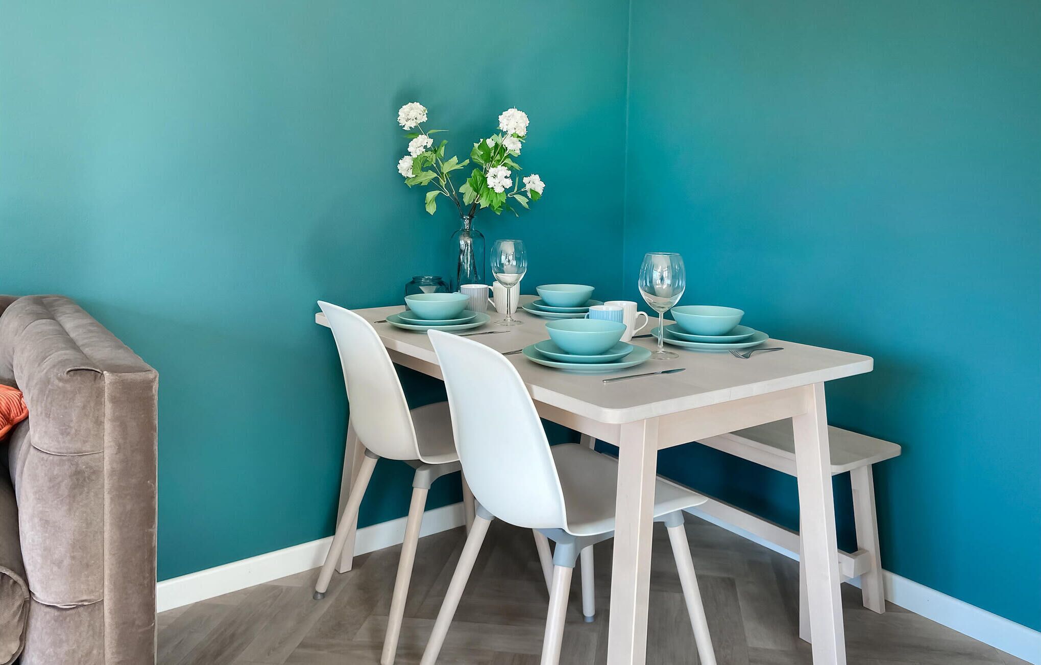 A dining area with a teal wall, a white table, and matching chairs.