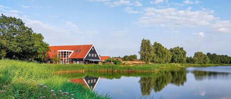 A house with a red roof and a pond in front.