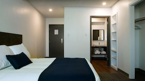 Habitació d'hotel amb llit, porta, bany amb rentaplat i mirall, i un vestidor.