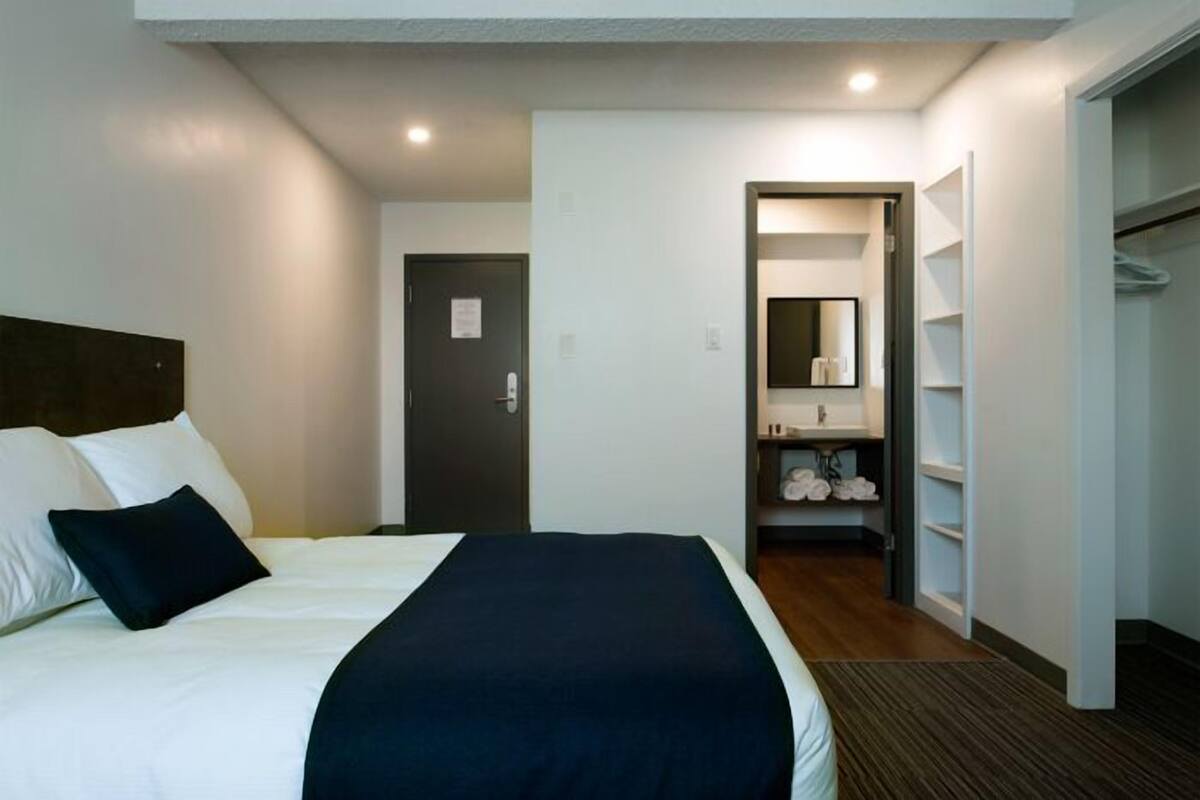 A hotel room with a bed, a door, a bathroom with a sink and mirror, and a walk-in closet.