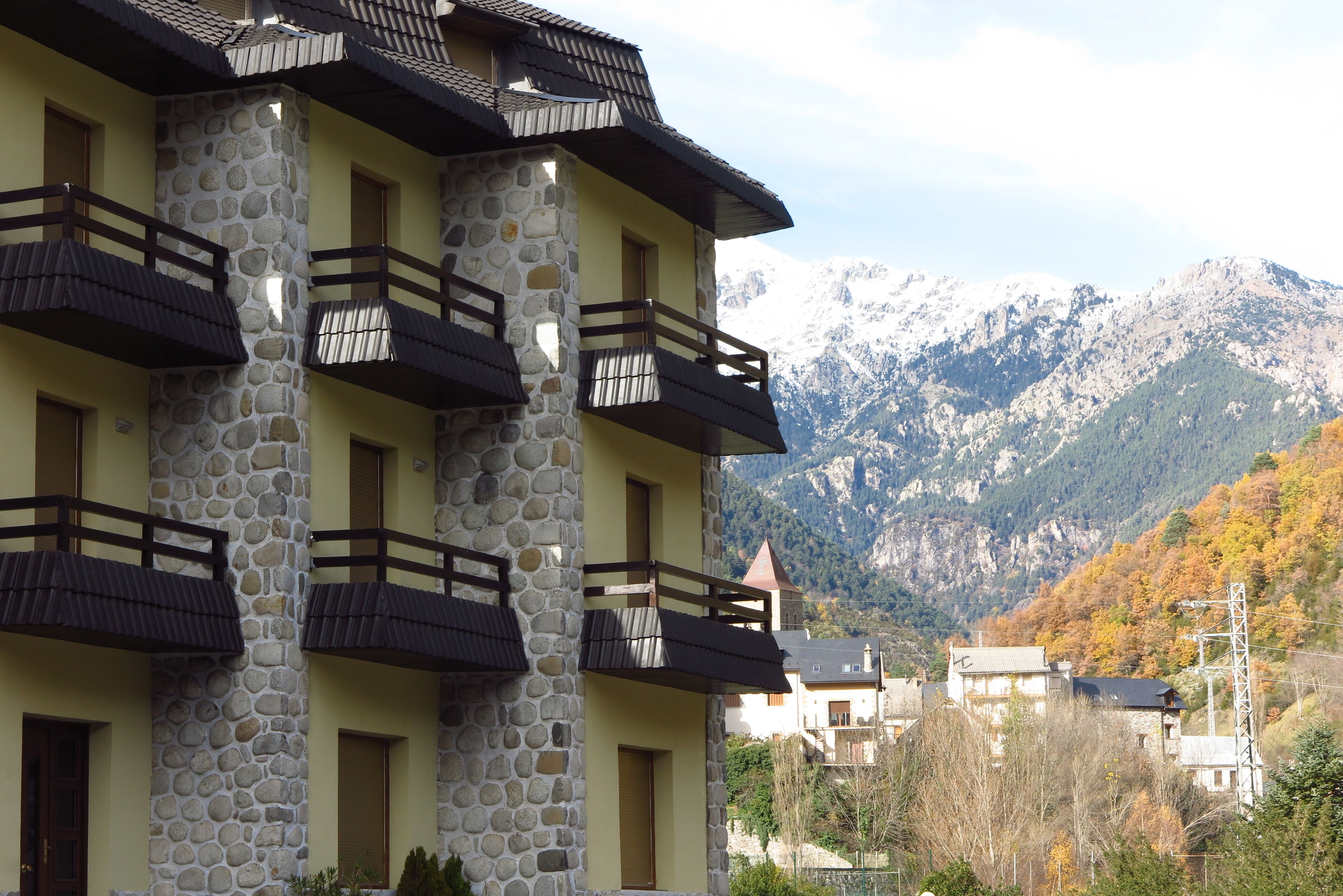 Un edificio de varios pisos con fachada de piedra y balcones, frente a un telón de fondo montañoso.