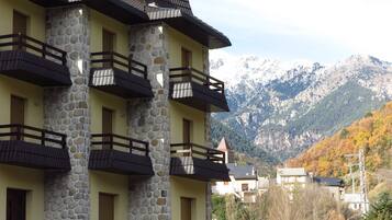 Un edificio de varios pisos con fachada de piedra y balcones, frente a un telón de fondo montañoso.