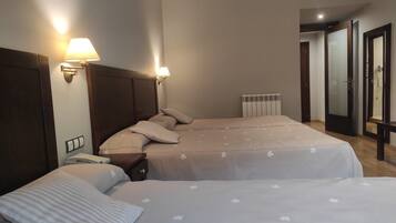 Habitación de hotel con dos camas, una mesita de noche, una lámpara, un radiador y un espejo.