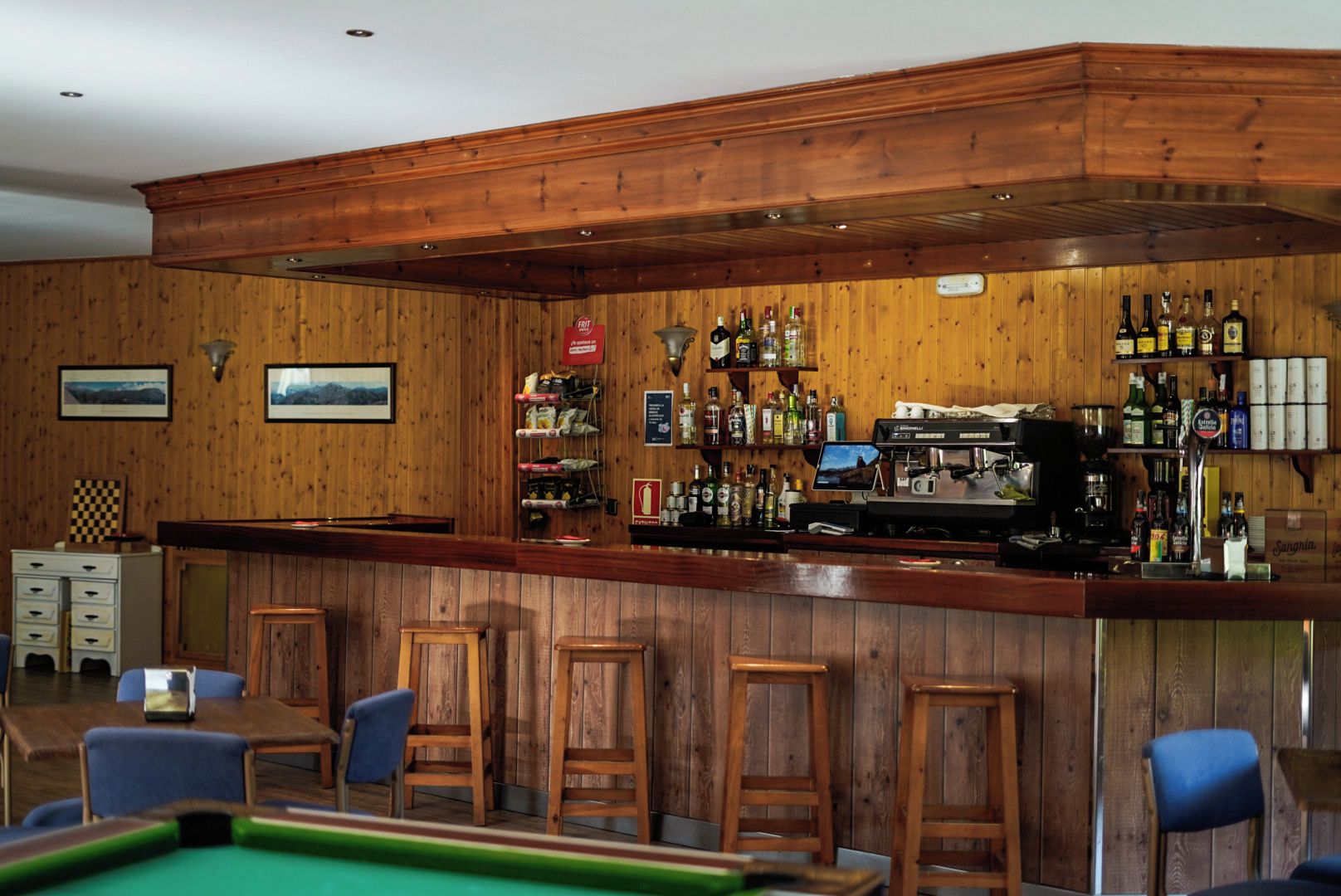 A bar area with wooden paneling, a pool table, and bar stools.