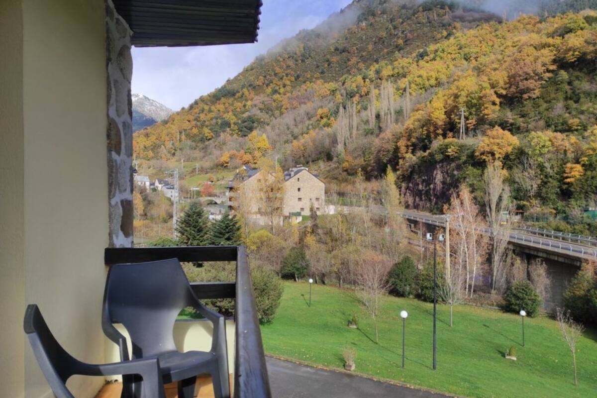 A balcony with a view of a mountainous landscape, a stone wall, and a chair.