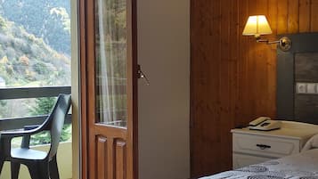Un dormitorio con cama, una mesita de noche con lámpara, una silla y vistas a un área boscosa a través de un ventanal.