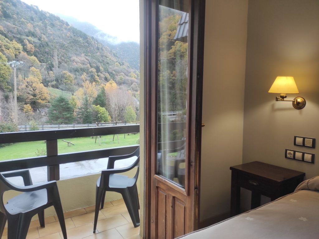Un balcón con vistas a un paisaje montañoso, una mesita y una cama con una mesita de noche.