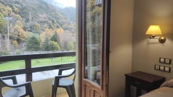 Un balcón con vistas a un paisaje montañoso, una mesita y una cama con una mesita de noche.