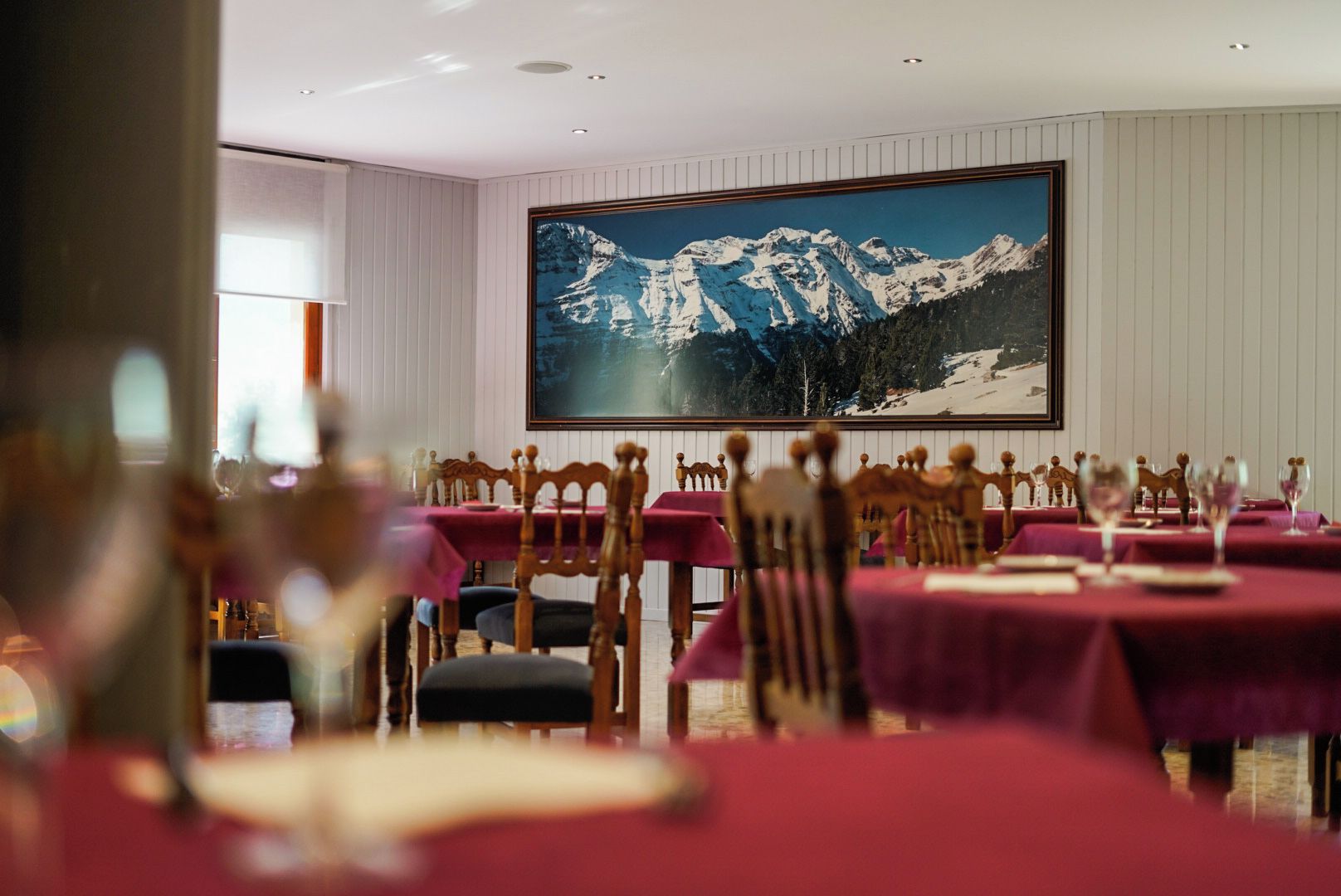 Un comedor con mesas dispuestas para comer, sillas y un cuadro grande enmarcado con un paisaje de montaña en la pared.